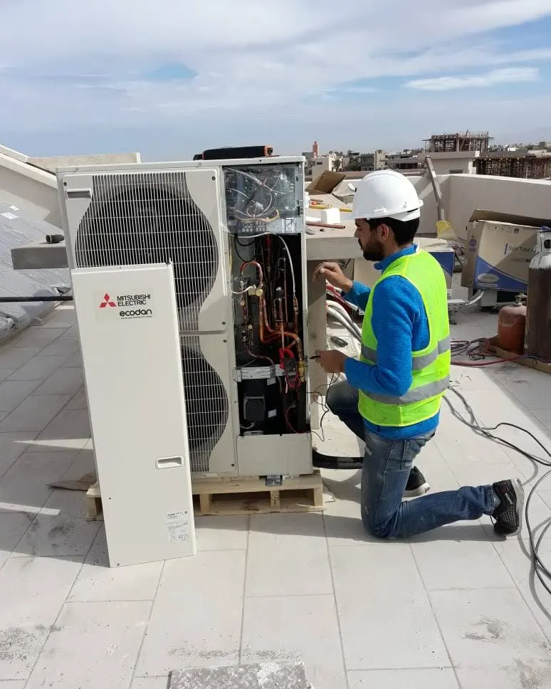Technician servicing a Mitsubishi Electric heat pump on a rooftop