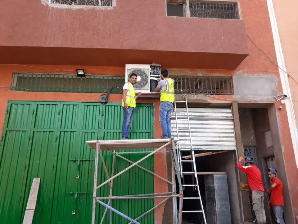 Techniciens posant une unité extérieure de climatisation en façade depuis un échafaudage
